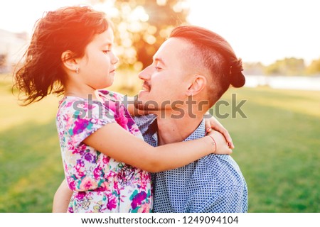 Closeup portrait of happy smiling father holding, hugging, playing, having fun with his cheerful laughing, smiling funny pretty daughter outdoor in summer.  Dad loves his female child. Family in park