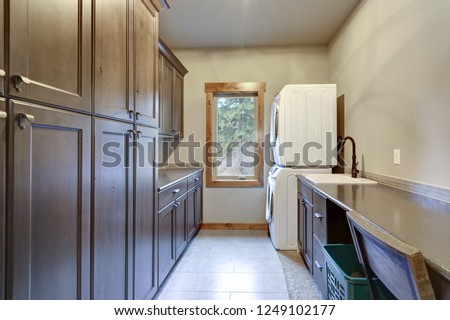Laundry room with a stacked white front loading washer and dryer, floor to ceiling dark shaker cabinets.