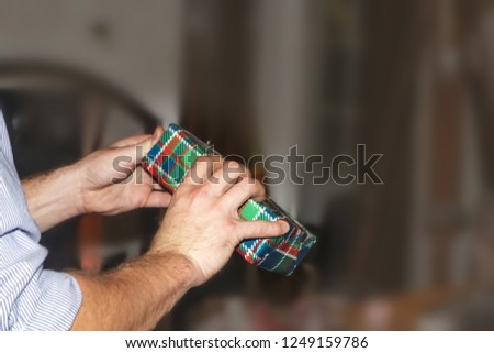 Man's arms and hands opening plaid wrapped Christmas present against very blurred background - room for text