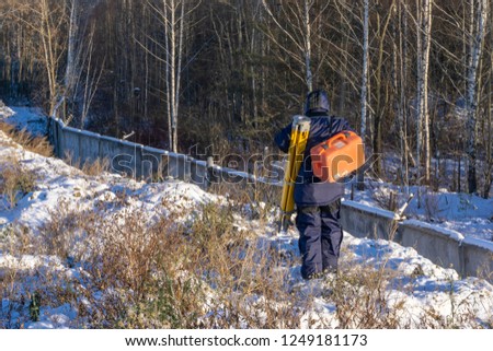 Surveyor comes with a tripod and gauge in winter at a construction site