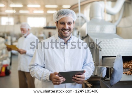 Smiling young technologist using tablet. Food factory interior.