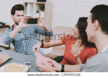 Young Smiling People Taking Photo on Party at Home. Man with Smartphone. Indoor Fun. Young Smiling Girl. Young Smiling Guy. Sitting at Table. Party with Friends. Indoor Activities Concept.