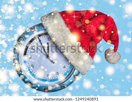 Concept: Christmas and New Year. Santa's hat is worn on wall clock and arrows show  approaching New Year's midnight on blue background, golden falling snow