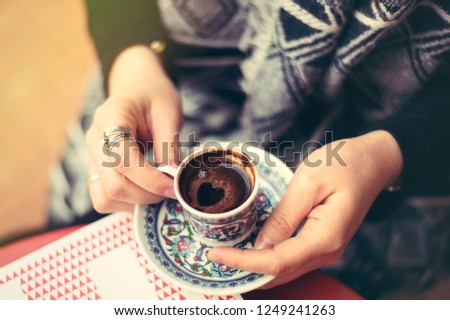 Top view to turkish coffee in tradition coffee cup with ornaments in woman's hands. Heart shape
