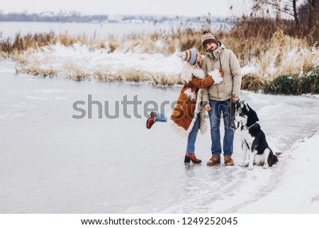 Style young couple having fun in winter park near lake with their friend husky dog on a bright day hugging each other and smiling 