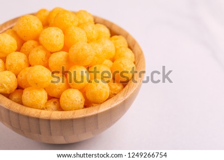Cheese puff balls in wooden bowl on light background. Cinema snacks. Copy space