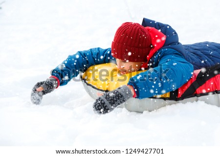 Happy cute excited boy teenager  sledding downhill on a snowy day. winter activity active leisure and entertainment concept.