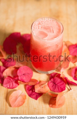 Glass of fresh pink Watermelon Juice surrounded by bougainvillea petals.