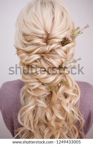 Back view of an elegant trendy hairstyle, interlacing curls and decorating with flower petals. Beautiful and well-groomed blonde hair