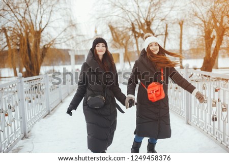 Two stylish girls walking in a winter snowy park