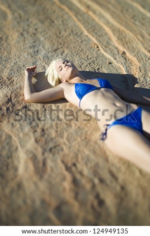 Blonde woman in bikini lying on cliff on seashore