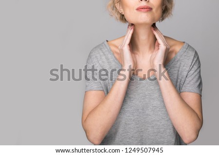 Female checking thyroid gland by herself. Close up of woman in white t- shirt touching neck with red spot. Thyroid disorder includes goiter, hyperthyroid, hypothyroid, tumor or cancer. Health care. Royalty-Free Stock Photo #1249507945