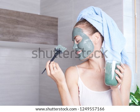 Woman applying mask moisturizing skin cream on face looking in bathroom mirror. Girl taking care of her complexion layering moisturizer. Skincare spa treatment