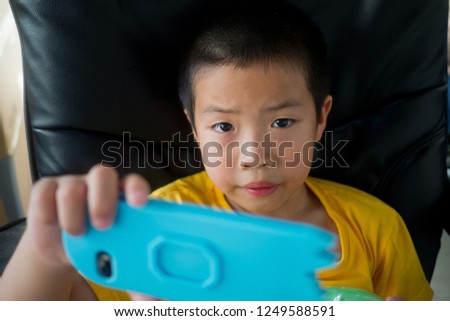 asian chinese boy playing smartphone on bed, watching smartphone, kid use phone and play game, child use mobile, addicted game and cartoon,
