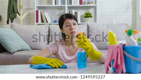 Exhausted asian housewife looking outside the house from window to the urban city view. young lady sitting on floor resting while doing housework wiping table. elegant woman wearing gloves cleaning.