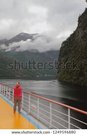 Woman photographs fjord from deck of cruise liner. Geirangerfjord, Stranda, Norway