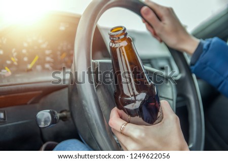 Drunk girl drives a car with a bottle of alcohol in her hand. The girl holds the wheel and a bottle of beer.