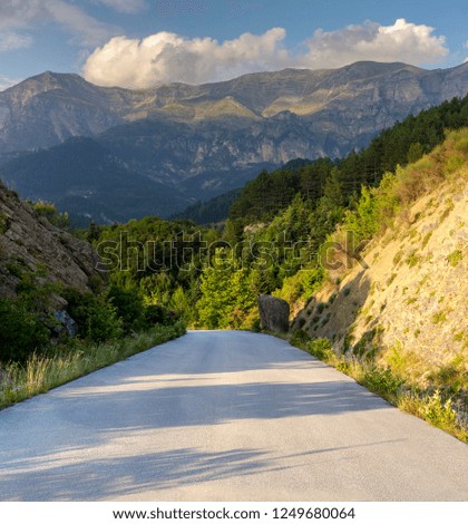 View of a rural, narrow road and mountains at sunset in summer (region Tzoumerka, Epirus, Greece).