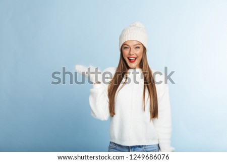 Excited young woman wearing sweater and hat isolated over blue background, presenting copy space