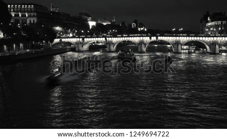 Night view of Seine river with Pont Neuf bridge, touristic ship and two police boats coming. Paris, France. Black and white photo.