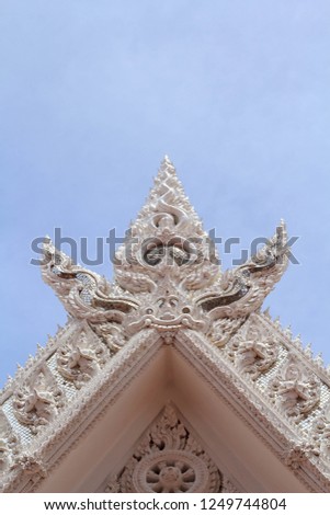 high and low relief sculpture is an artistic artist designed with marble on the pediment of the white Thai temple church in the form of a beautiful Naga with a blue sky background.