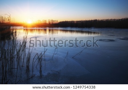 Winter landscape with frozen river, reeds and sunset sky. Daybreak