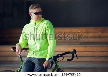 Photo of man in sunglasses standing with bicycle indoors