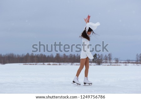 Beautiful young woman on skates in white dress outdoors at winter snow