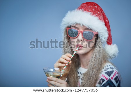 Christmas or New Year celebration. Closeup of frozen girl with snow on face wearing Santa hat and sunglasses, drinking through a straw, portrait with copy space