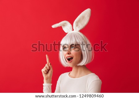 Image of an excited young shocked woman dressed in carnival christmas bunny costume posing isolated over red wall background.