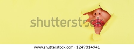 Beauty salon advertising banner with copy space. View of bright lips with glitter through hole in yellow paper background. Make up artist, beauty concept. Cosmetics sale.