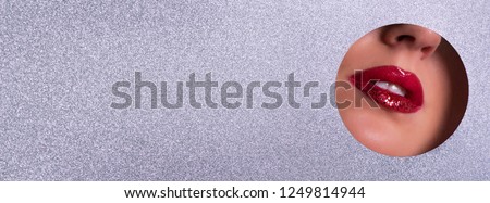 Beauty salon advertising banner with copy space. View of bright lips with glitter through hole in silver paper background. Make up artist, beauty concept. Ready to new year party. Cosmetics sale
