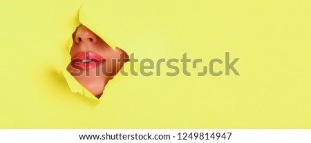 Beauty salon advertising banner with copy space. View of bright lips with glitter through hole in yellow paper background. Make up artist, beauty concept. Cosmetics sale.
