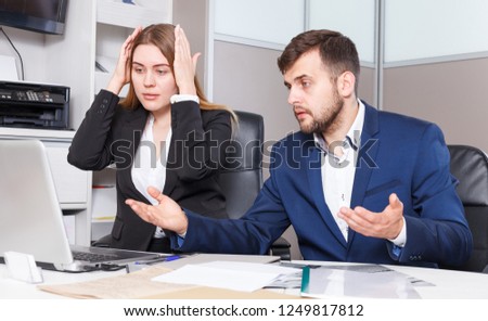 Portrait of worried young salespeople working on laptop in furniture showroom
