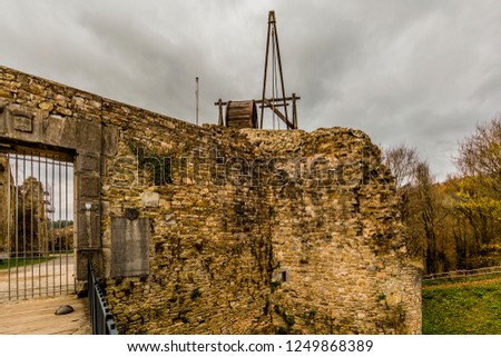 Deteriorated brick walls of the Franchimont castle ruins, wooden wheel crane, bare trees in autumn in the background, cloudy day with a stormy gray sky in Theux, Belgian Ardennes