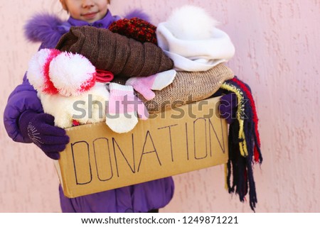 Girl holding donation box with warm winter clothes. 