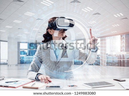 Conceptual image of confident and successful business woman in suit sitting inside office building with security interface and using virtual reality headset