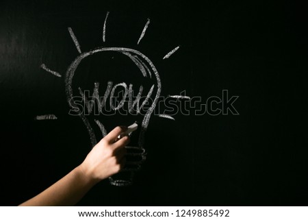 closeup female hand drawing a white chalk light bulb on a black board with the word wow.