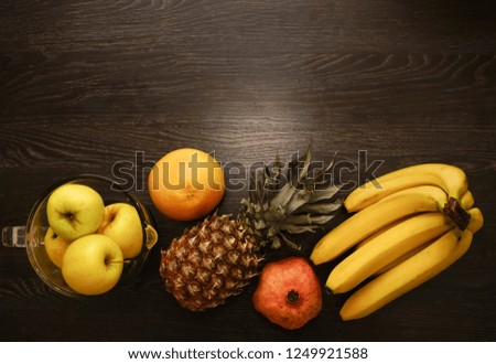full blender with yellow apples near standing one pineapples, grapefruit, pomegranate and fresh bunch of bananas. top view. black wooden table background.empty copy space. row healthy food