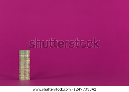 Single stack of gold coloured coins on a vibrant pink / purple coloured background. Positioned left with copy space and natural shadow. £2 UK sterling coins. Royalty-Free Stock Photo #1249933342