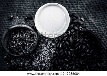 Close up of paste of custard apple seeds in a glass bowl with some powdered seeds and raw dried seeds on brown colored surface.