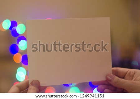 christmas mockup card with space for text. hand holding empty greeting card on bokeh background of lights. cozy winter holidays.