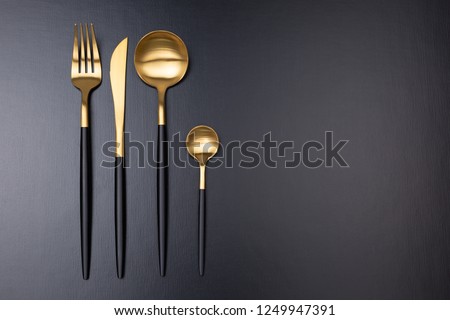 Set of stylish black and gold cutlery on black background. Dark and moody vibes. Fashionable and luxury eating. Flat-lay, top view. Copy space for your text. Royalty-Free Stock Photo #1249947391