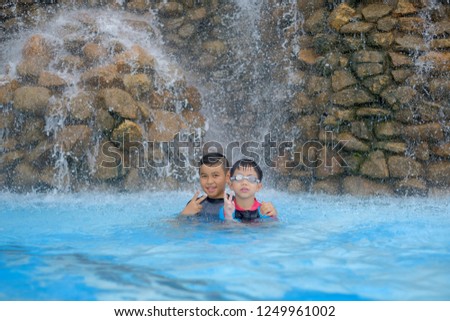 Asian children in swimming suit smiling showing and pointing up with fingers number two while smiling confident and happy in water park.