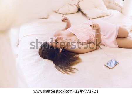 Woman in a pink dress with headphones listening to music lying next to a mobile phone