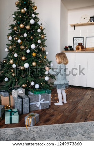 Merry Christmas and Happy Holidays! Cute little child girl is decorating the Christmas tree indoors.