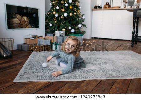 Girl playing with Christmas decoration. Christmas gift boxes and tree on background

