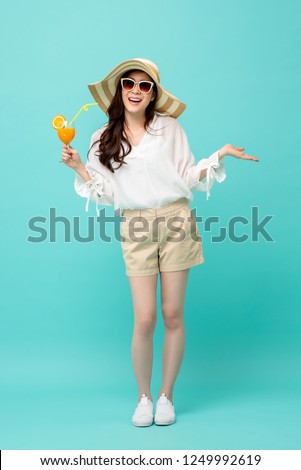 Happy Asian woman in summer casual clothes holding a glass of fruit juice drink studio shot isolated on light blue backgroud