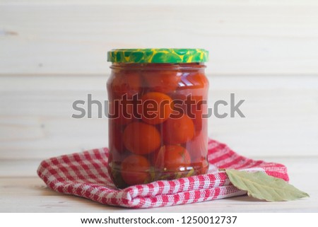 Salted red tomatoes in a jar on a red napkin on a light wooden background. Fermented vegetables.