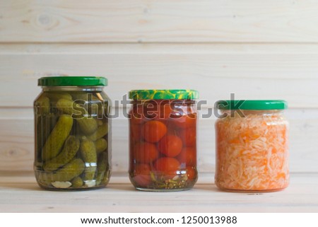 Gherkins, tomatoes and sauerkraut in jars on a light wooden background. Fermented vegetables.